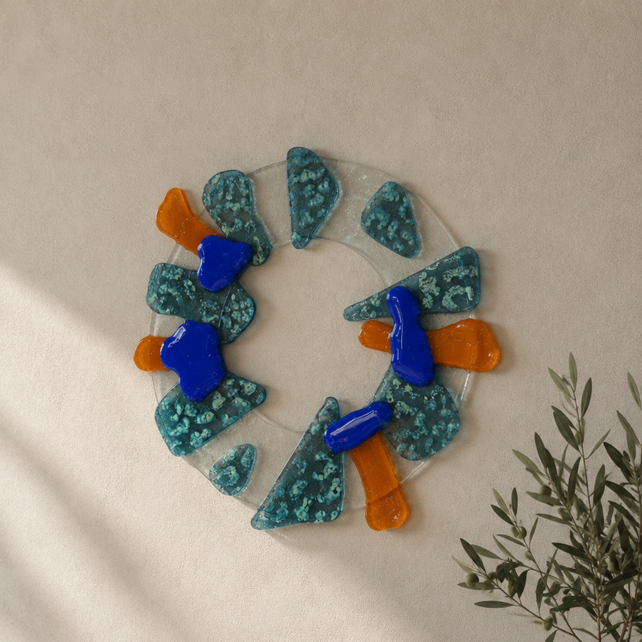 Fused glass wreath with orange and blue accents, displayed on a wall